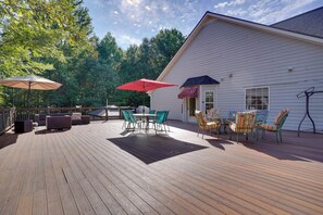 Eine Holzterrasse mit Gartenmöbeln, darunter Stühle und ein Tisch, sowie zwei Sonnenschirmen.