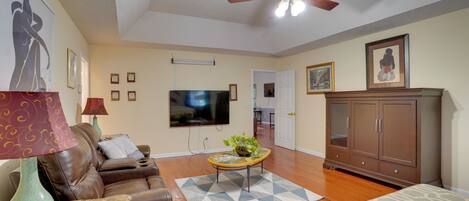 A living room with a ceiling fan, a flat-screen TV, a brown leather sofa, a coffee table with books, and a patterned rug.