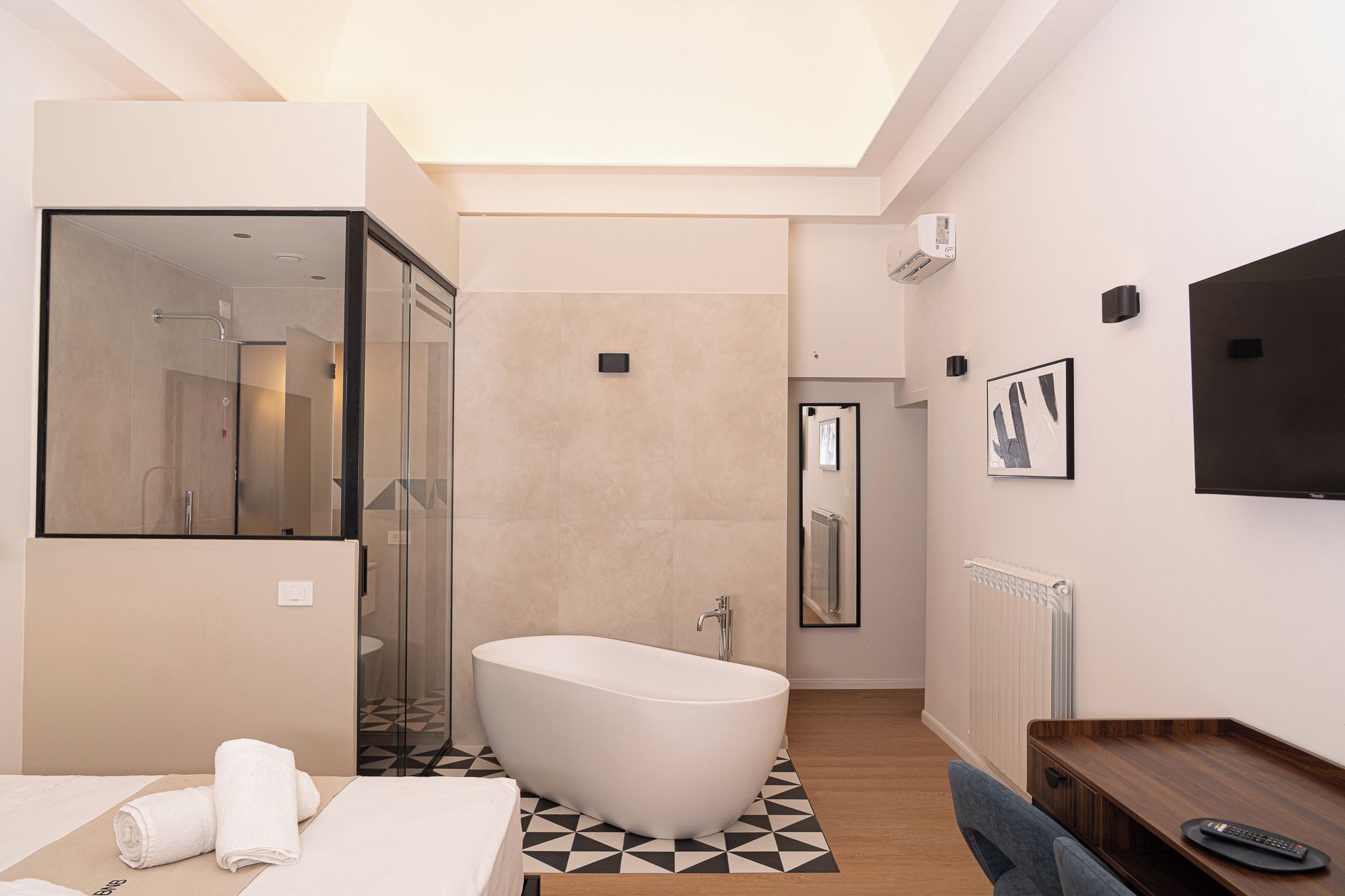 Un baño moderno con una bañera independiente, cabina de ducha con paredes de vidrio y un tocador de madera con espejo.