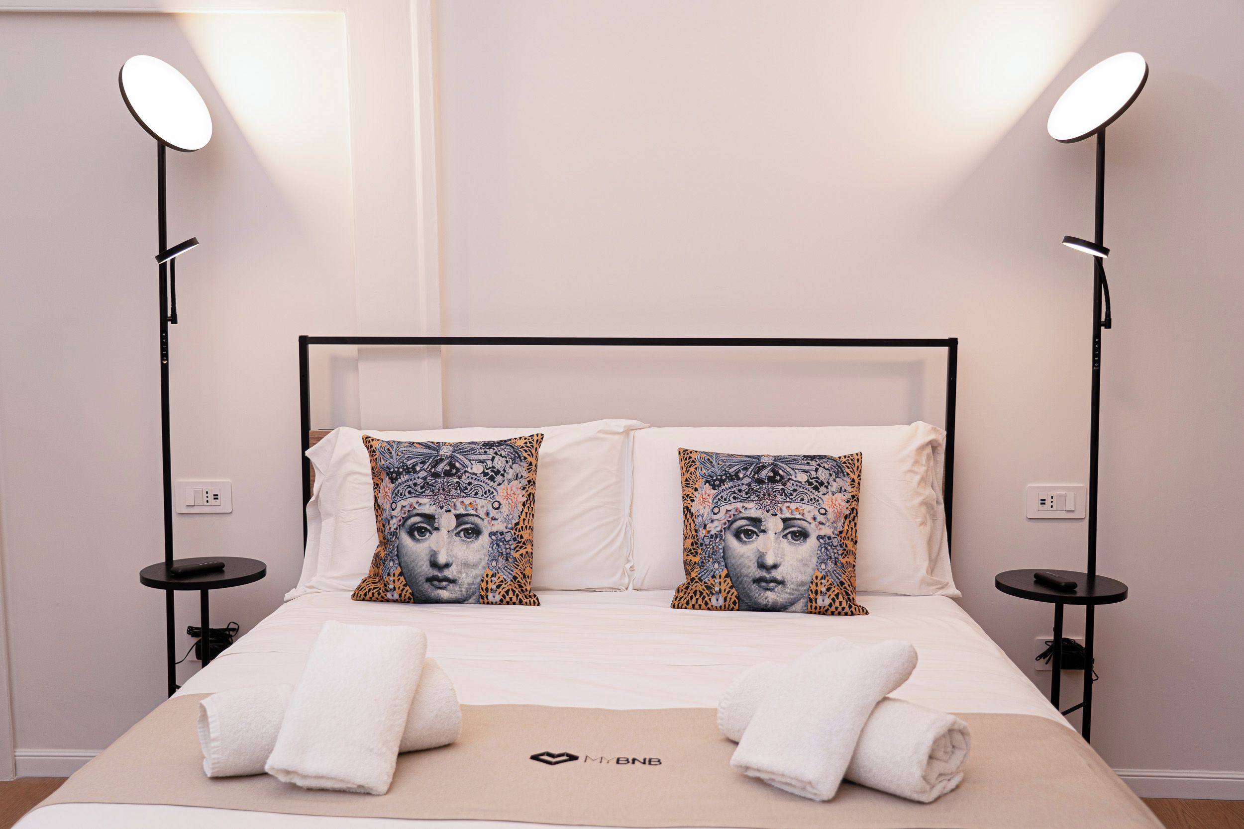Habitación de hotel con una cama, dos lámparas de noche, una mesita de noche y un enchufe de pared.