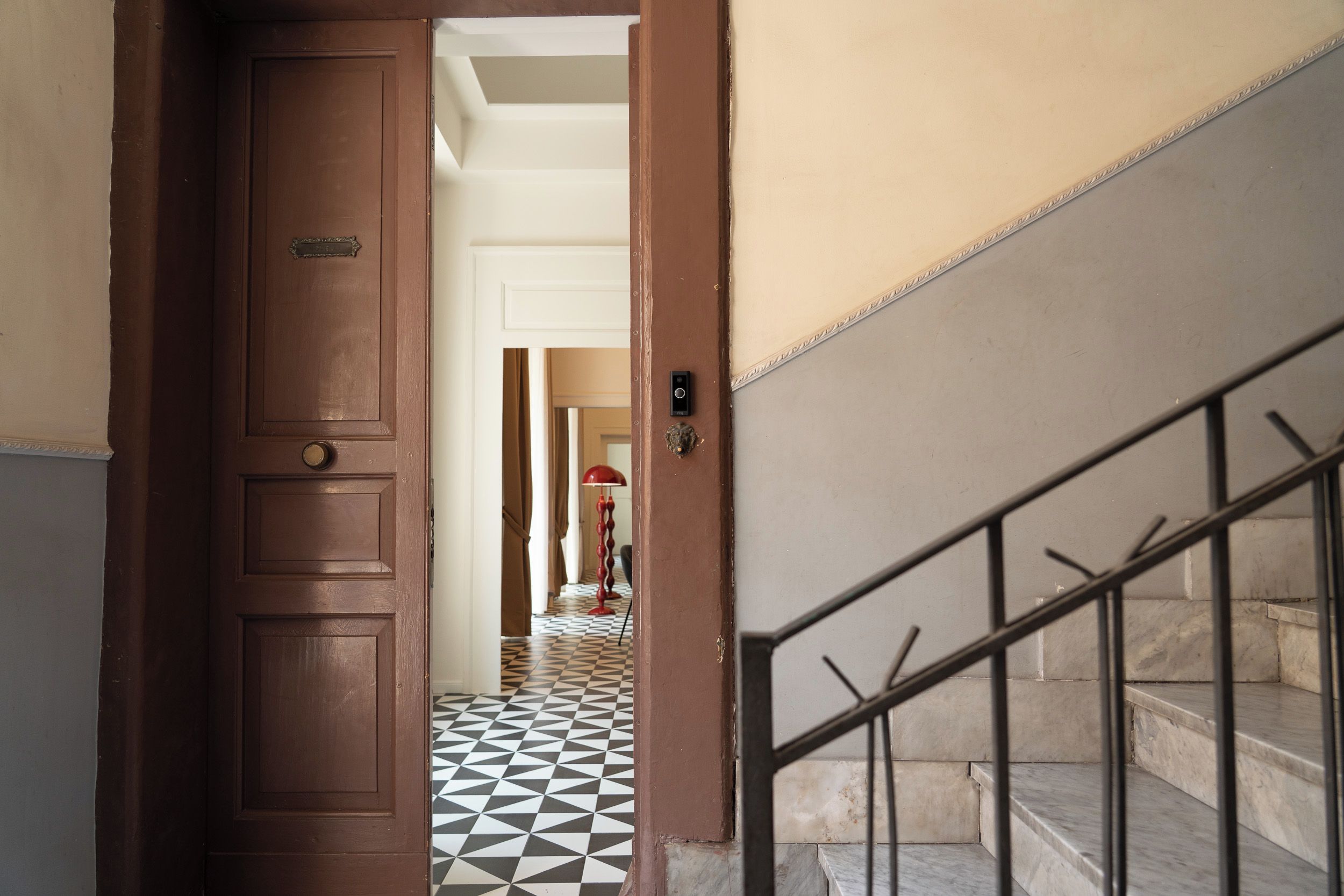 Un couloir avec une porte en bois, un sol carrelé et un escalier doté de rampes en métal.