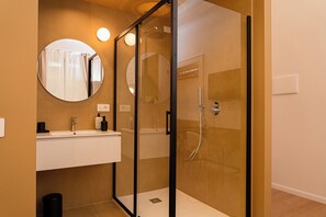 Een moderne badkamer met een douchecabine van glas, een ronde spiegel en een witte wastafel met toiletartikelen.