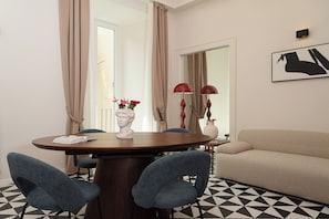 A dining area with a round table, two chairs, a vase with flowers, and a sofa. - Tempora Domus E' (Naples)
