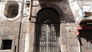 A building facade with a metal gate, a small window, and a door with a fanlight. - Tempora Domus E' (Naples)