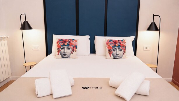 A neatly made bed with two pillows, two bedside lamps, and a pair of towels on the floor. - Tempora Domus E' (Naples)