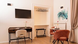 A hotel room with a desk, two chairs, a television, a coat rack, and a radiator. - Tempora Domus E' (Naples)