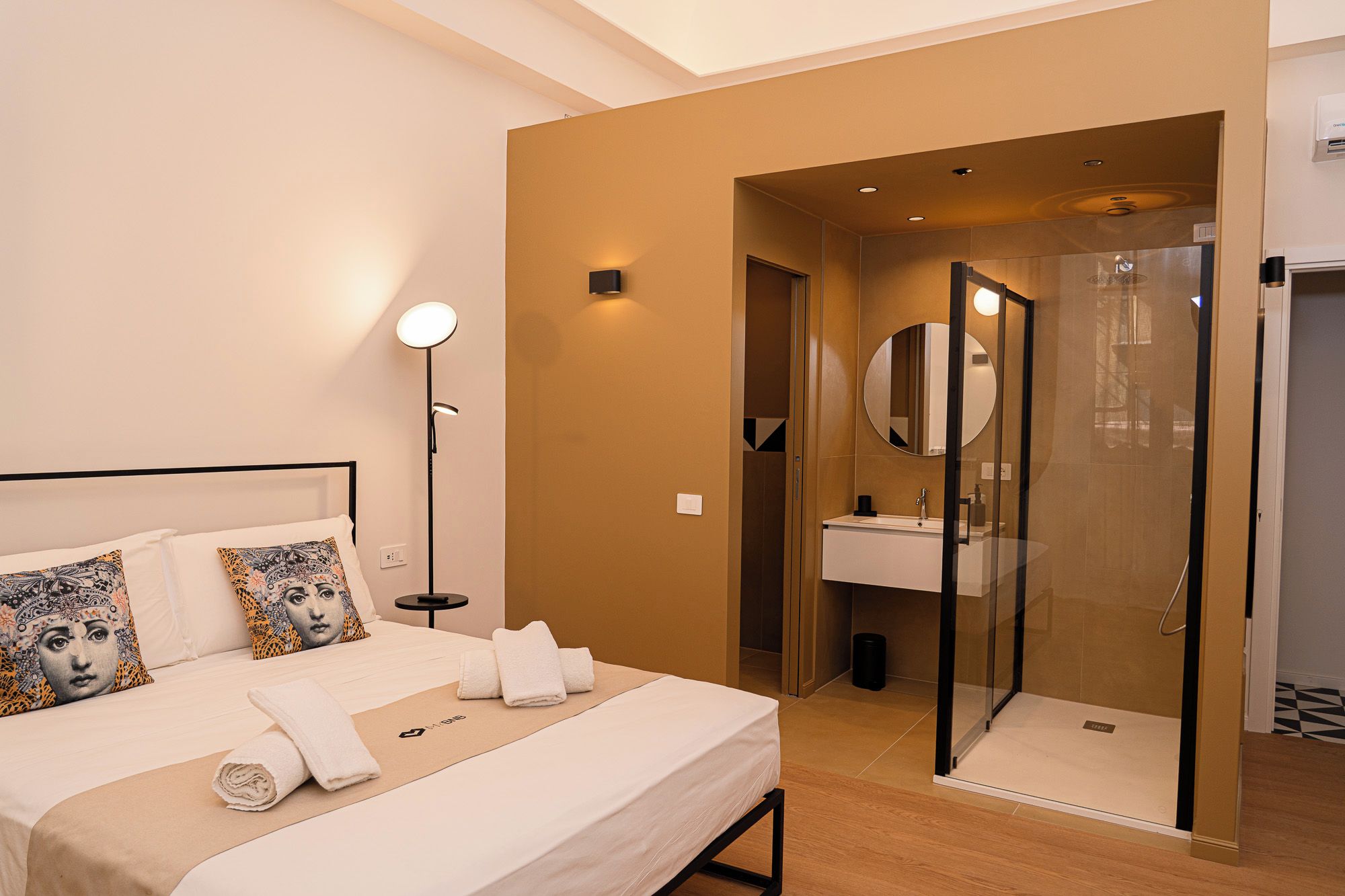 A hotel room with a bed, bedside lamp, and a bathroom with a shower and sink.