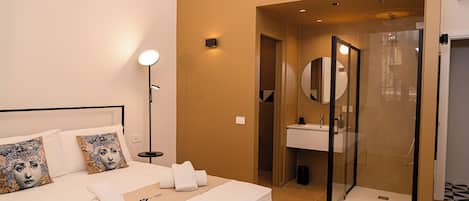 A hotel room with a bed, bedside lamp, and a bathroom with a shower and sink.
