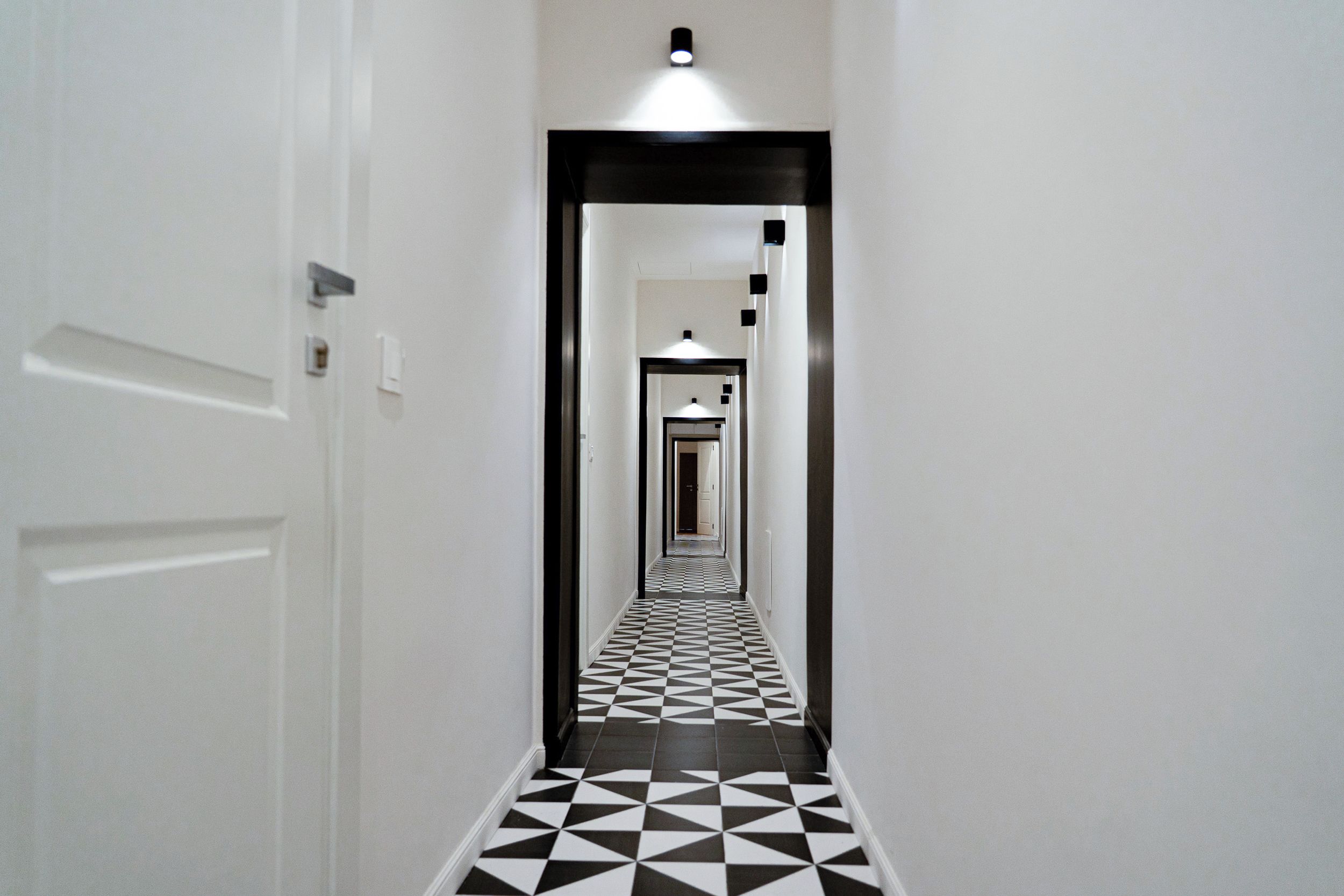 A hallway with a checkered floor pattern, white walls, and a door on the left.