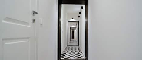 Un pasillo con piso a cuadros, paredes blancas y una puerta a la izquierda.