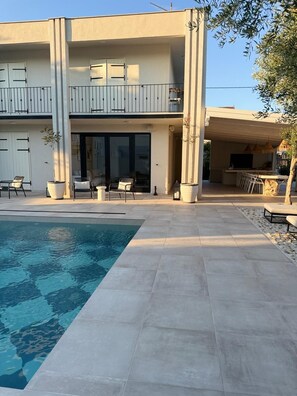 Un bâtiment moderne à deux étages doté d’une piscine, d’un espace extérieur aménagé et d’un patio couvert.