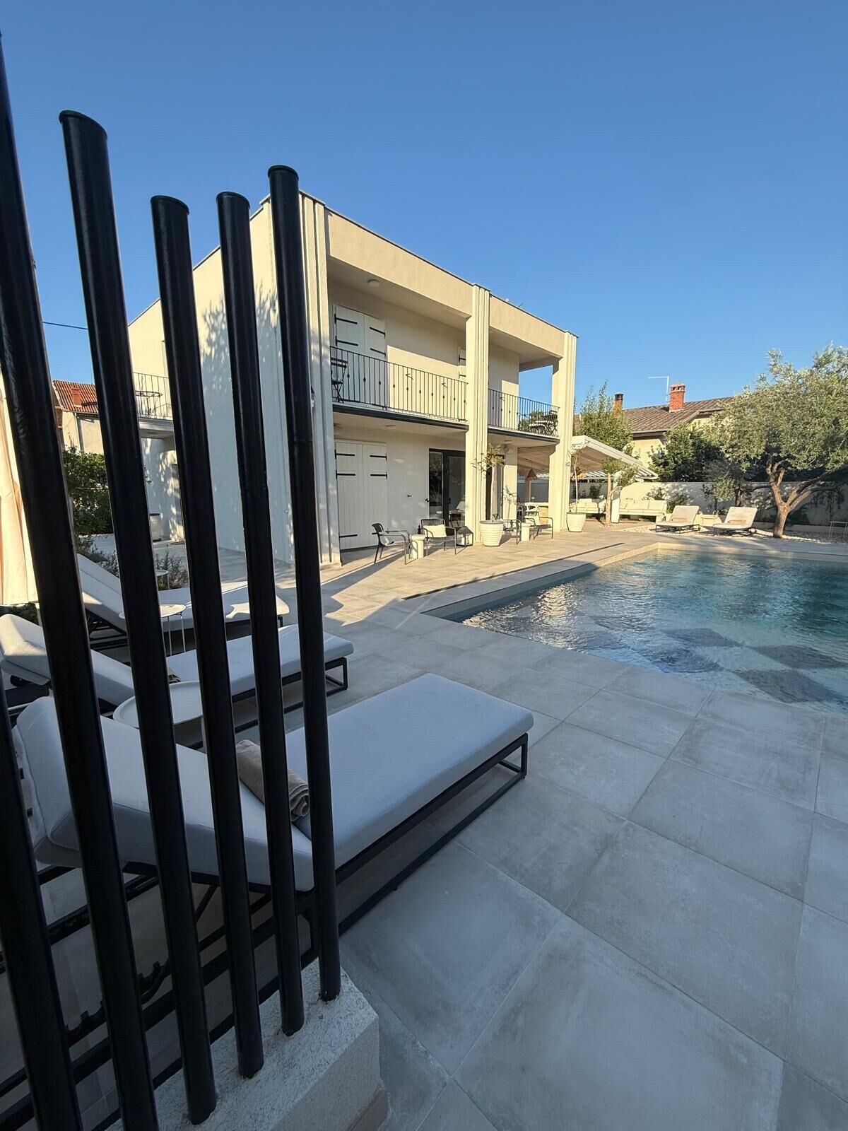 Zona de piscina amb gandules, cel blau i un edifici modern amb un balcó.