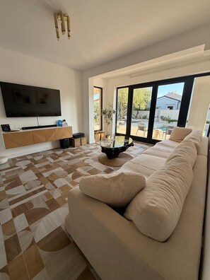 Ein modernes Wohnzimmer mit einem großen Flachbildfernseher, einem beigen Sofa und einem gemusterten Teppich.