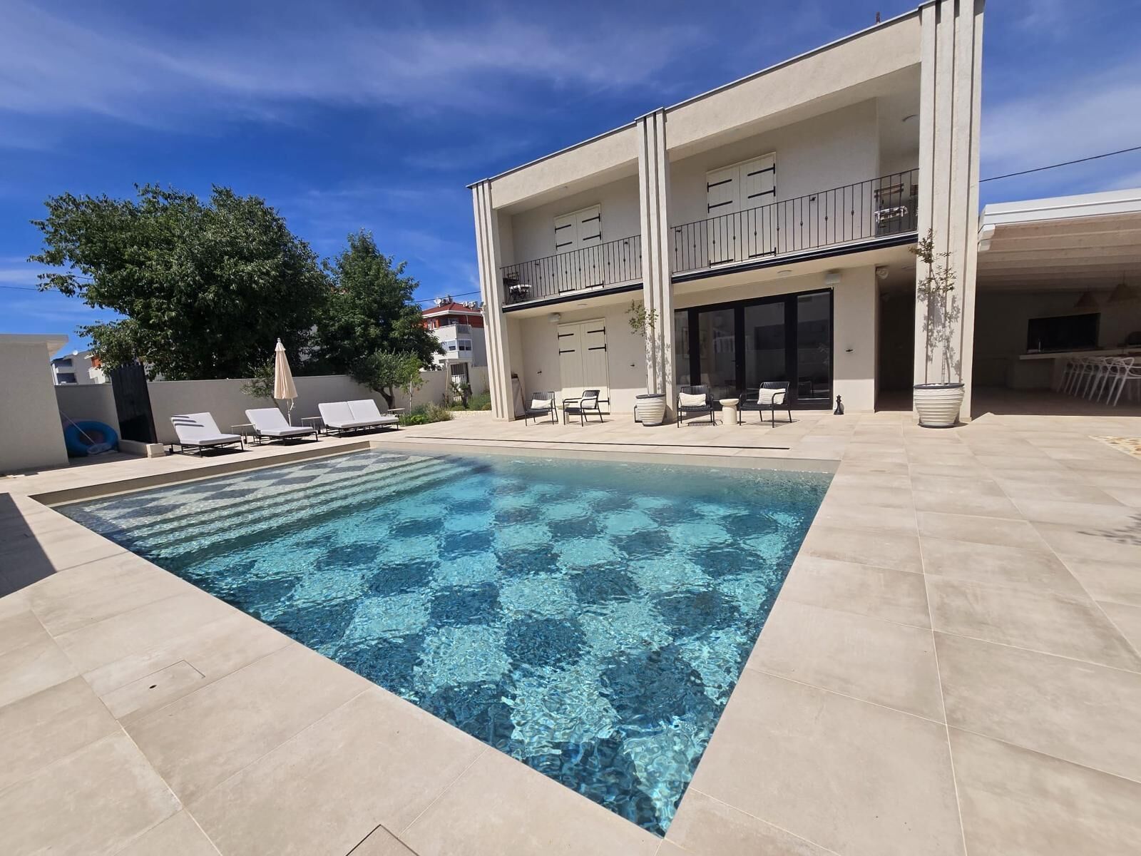 A rectangular swimming pool with clear blue water, surrounded by a tiled deck.