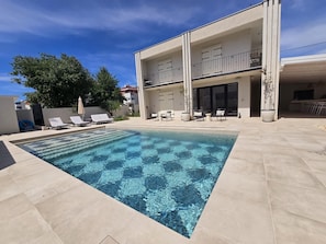 Uma piscina retangular com água azul cristalina, rodeada por um deck revestido com azulejos.