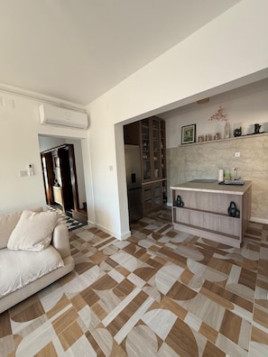 Un salon moderne avec un canapé, un coin cuisine doté d’un plan de travail en marbre et un sol à motifs.