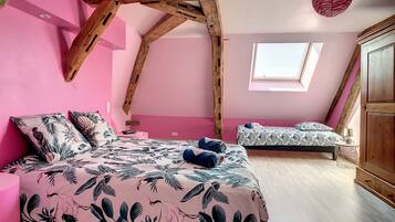 A bedroom with a sloped ceiling, a bed with a floral bedspread, a smaller bed, a window, and a wooden wardrobe.