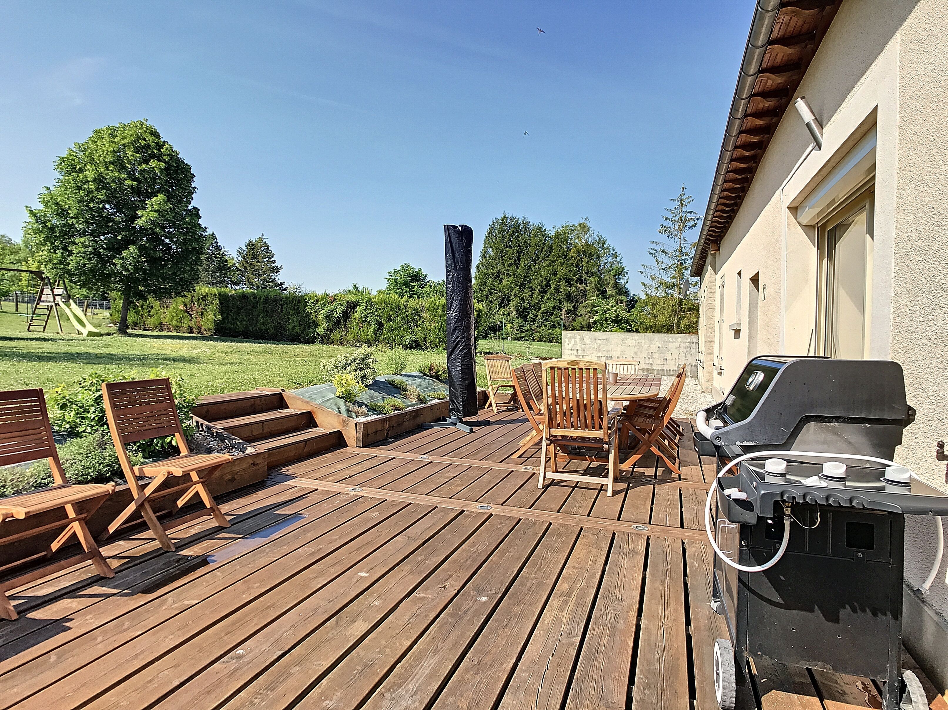 A wooden deck with outdoor furniture, a barbecue grill, and a garden area with a swing set.