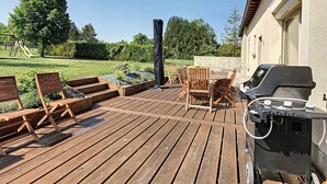 Een houten terras met buitenmeubilair, een barbecue en een tuin met een schommel.