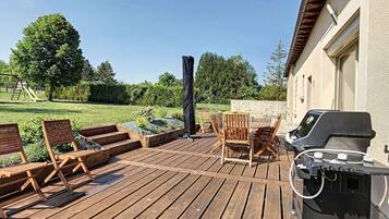 A wooden deck with outdoor furniture, a barbecue grill, and a garden area with a swing set.
