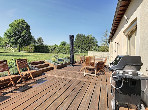 A wooden deck with outdoor furniture, a barbecue grill, and a garden area with a swing set.