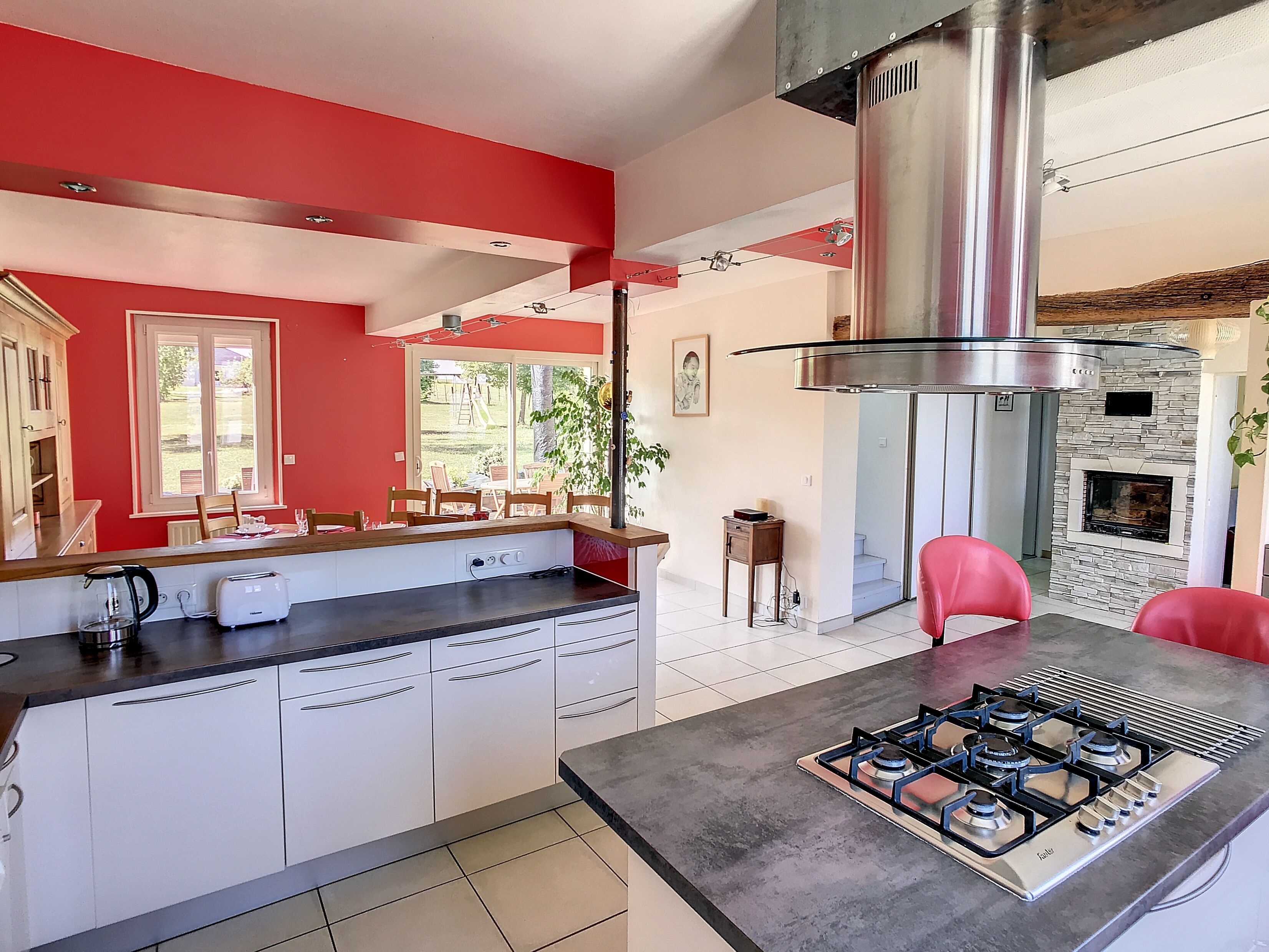 A modern kitchen with white cabinets, a gas stove, and a red accent wall.