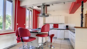 Een keuken met rode stoelen, een koffieapparaat en uitzicht op groen.