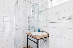 Ein modernes Badezimmer mit einer Duschkabine aus Glas, einem Holzausleger mit Waschbecken in Weiß und einem Spiegel über dem Waschbecken.