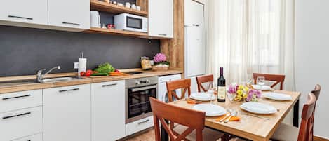 A modern kitchen with white cabinets, a wooden countertop, and a dining area with a wooden table set for four.