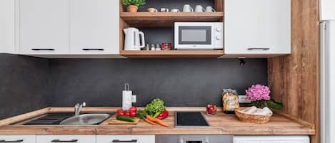A modern kitchen with white cabinets, a wooden countertop, a built-in microwave, a kettle, and a washing machine.