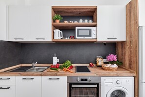 Eine moderne Küche mit weißen Schränken, einer Holzarbeitsplatte, einer eingebauten Mikrowelle, einem Wasserkocher und einer Waschmaschine.