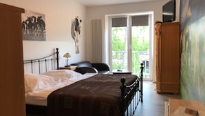 A bedroom with a bed, a chair, a nightstand, a TV, and a window with a view of greenery.