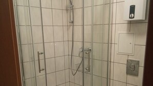 A corner shower enclosure with a glass door, a white toilet, and a wall-mounted control panel.