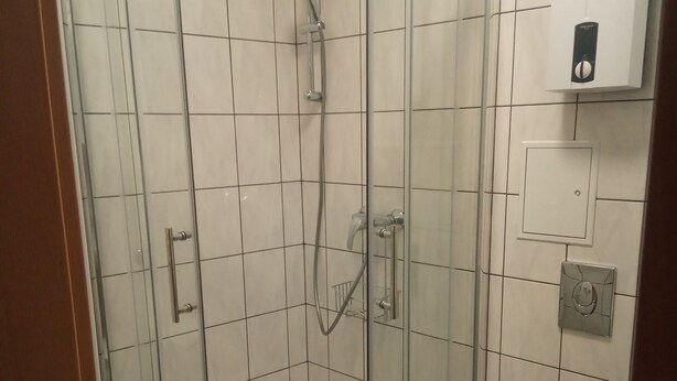Eine Eckdusche mit Glastür, eine weiße Toilette und eine an der Wand befestigte Bedienkonsole.