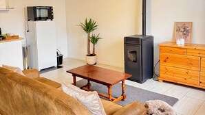 Ein Wohnzimmer mit einer Couch, einem Holztisch, einer Topfpflanze, einem Kamin und einer Küchenzeile mit Mikrowelle und Kühlschrank.