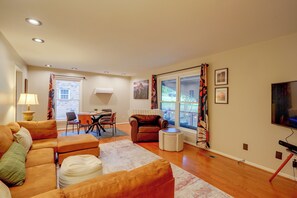 A living room with a sofa, chairs, a coffee table, a TV, and a dining area with a table and chairs. - Fire Pit & Grill! Wooded Durham Retreat (Durham)