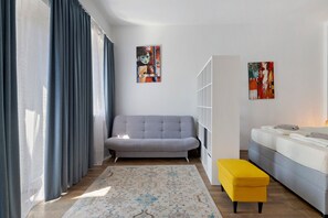 A modern living room with a grey sofa, a yellow ottoman, and two paintings on the wall.