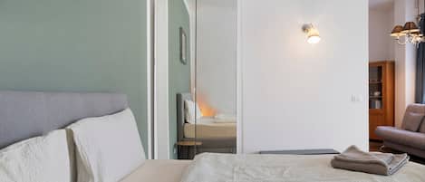 A bedroom with a bed, a bedside table, a lamp, and a view into another room.