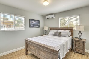 Une chambre à coucher avec un lit en bois, deux tables de chevet avec des lampes, une petite table et un climatiseur fixé au mur.