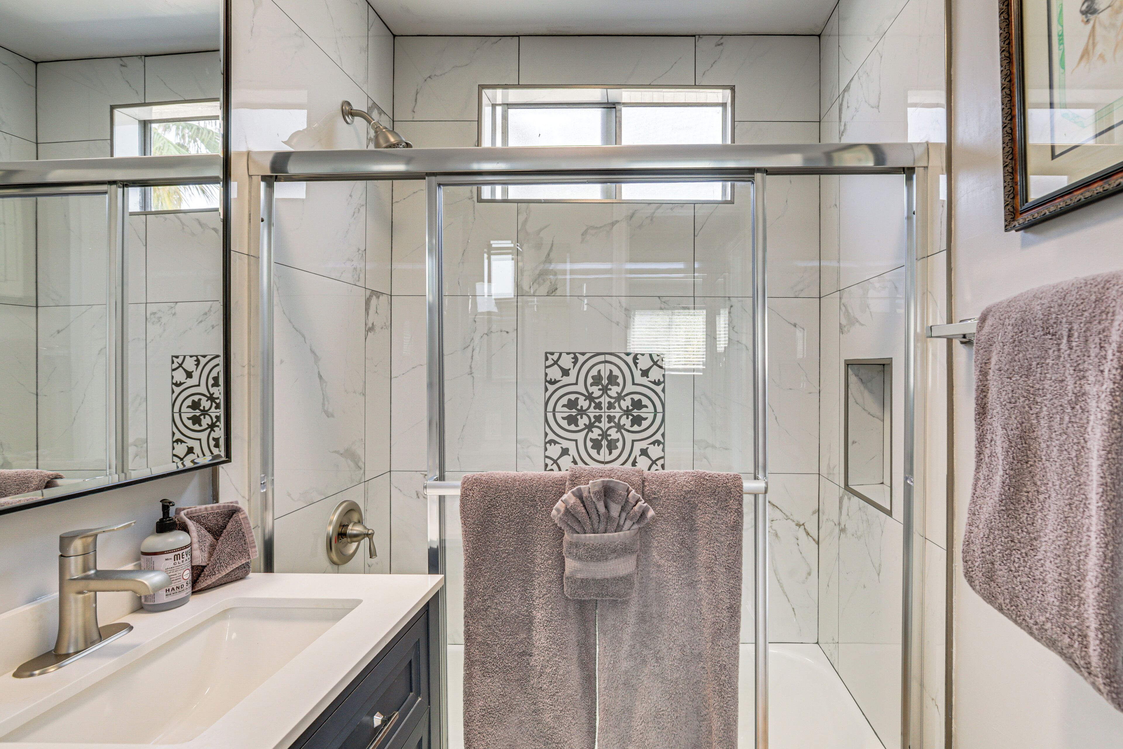 Un baño moderno con ducha de vidrio, tocador con espejo y perchero.
