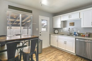 A kitchen with white cabinets, a wooden dining table with chairs, a window with blinds, and a kitchen island with a sink and countertop. - 5 Mi to SDSU & Trails! Stylish Apartment w/ Patio (La Mesa)