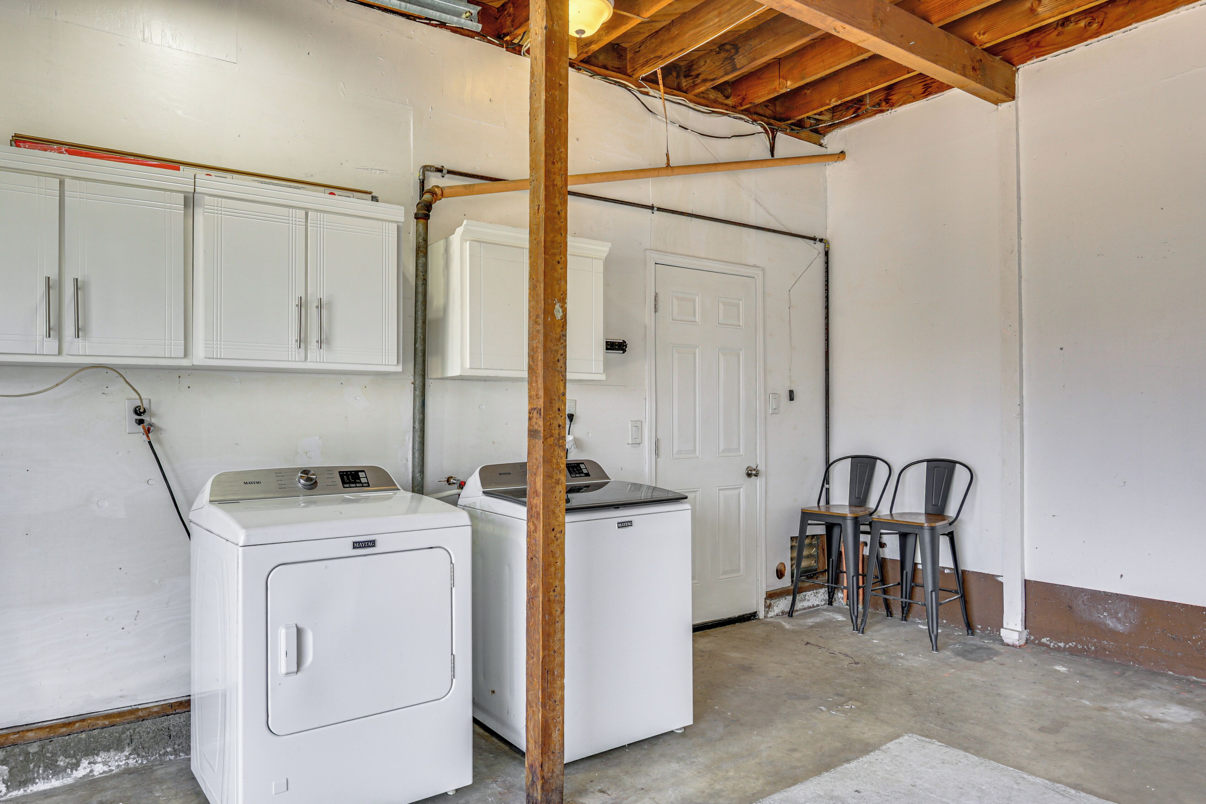 A laundry room with two white washing machines, a wooden beam ceiling, and a white door.