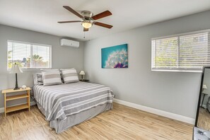 Ein Schlafzimmer mit einem Bett, Nachttischen, einem Deckenventilator und einem Fenster mit Jalousien.