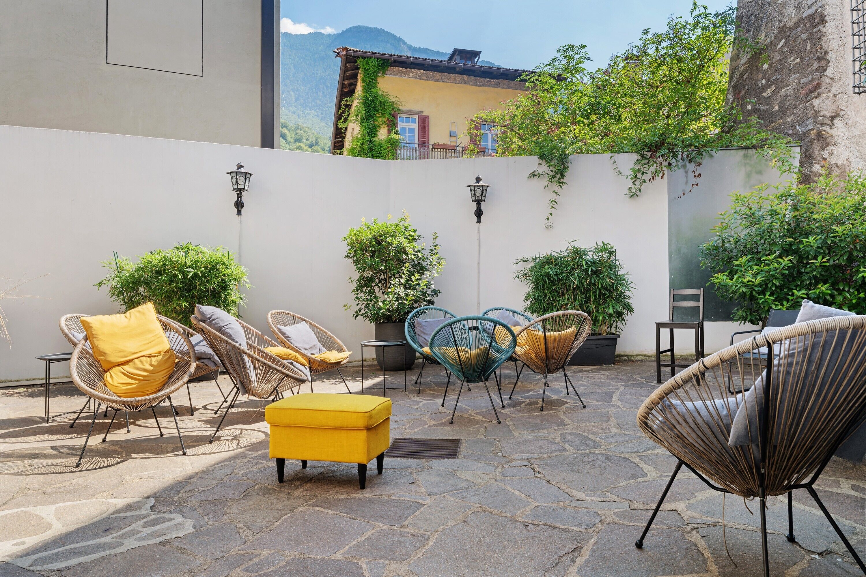 Un espace extérieur aménagé avec des chaises et des coussins en osier, un sol en pierre et des plantes en pot.