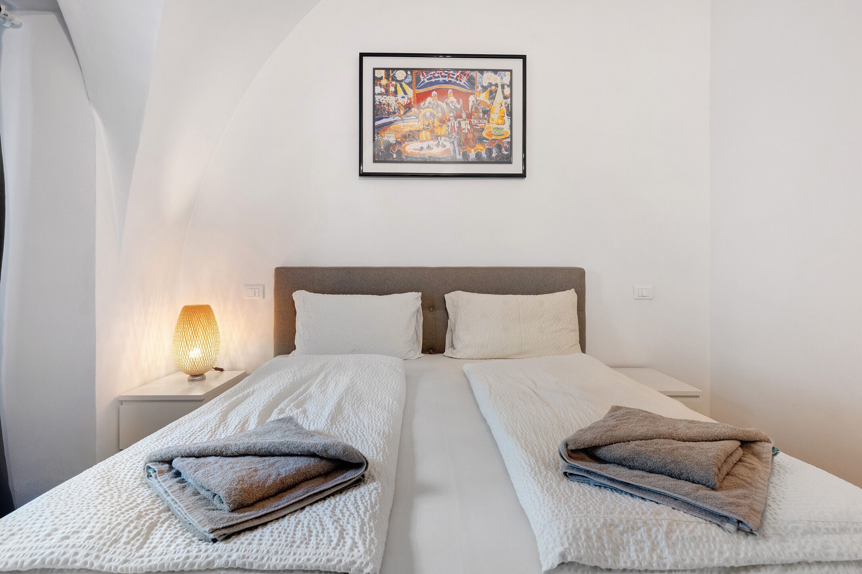 Une chambre d’hôtel avec deux lits, une table de chevet avec une lampe et un tableau encadré au mur.