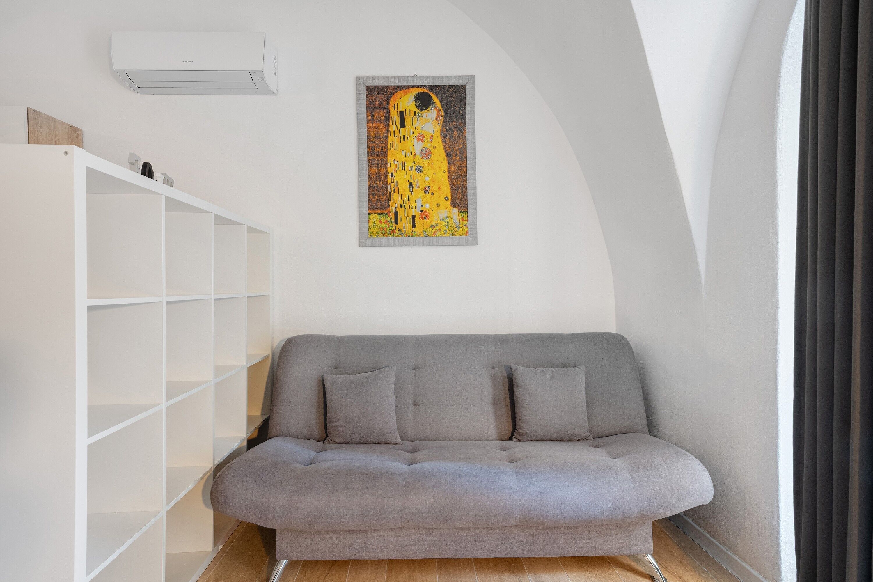 Un divano grigio con due cuscini, una scaffalatura bianca e un quadro appeso al muro.