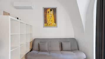 Un divano grigio con due cuscini, una scaffalatura bianca e un quadro appeso al muro.