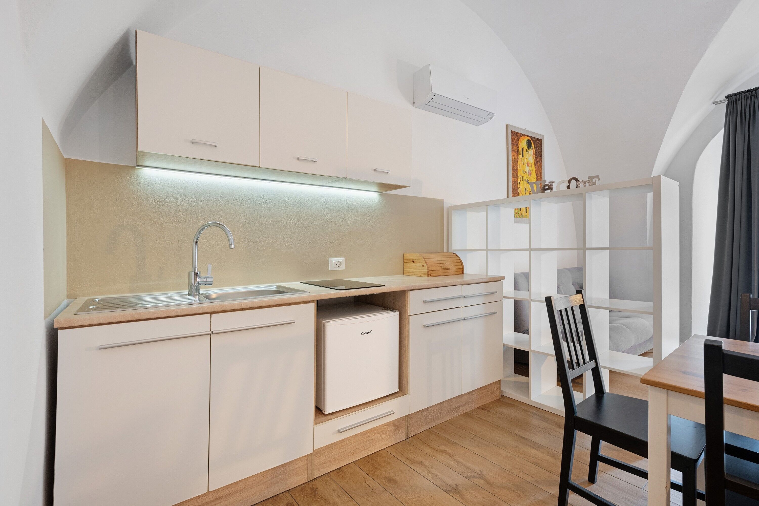 Une cuisine moderne avec des meubles blancs, un four encastré et une table à manger en bois, assortie de chaises.