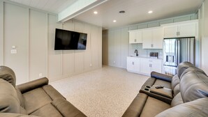 A modern living room with a flat-screen TV mounted on the wall, a seating area with a sofa and a coffee table, and a kitchen area with white cabinets and a refrigerator. - The Lily Pad - Nolin Lake Retreat (Clarkson)