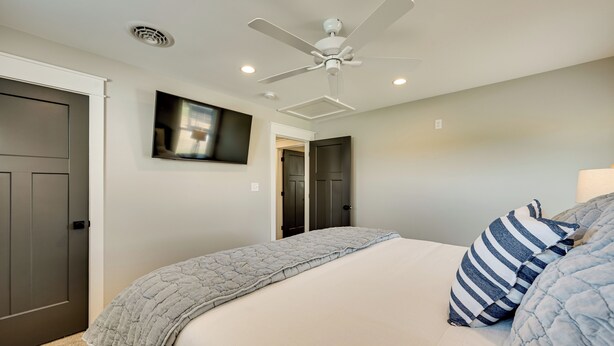 A bedroom with a bed, a ceiling fan, a TV mounted on the wall, and a door leading to another room. - The Lily Pad - Nolin Lake Retreat (Clarkson)